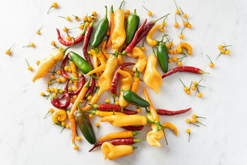 Bright yellow, green, and red chile peppers scattered on a white marble background