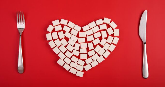Heart made by sugar cubes between fork and knife on red background. Flat lay video made by stop motion animation technic.