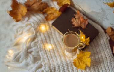 Autumn flat lay composition. Warm comfort white sweater, book, coffee cup, dried yellow leaves. Autumn, fall, slow living concept. Top view, copy space