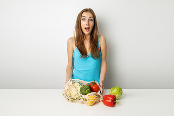 Surprised young woman with vegetables on table on white background