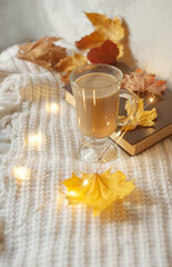 Autumn flat lay composition. Warm comfort white sweater, book, coffee cup, dried yellow leaves. Autumn, fall, slow living concept. Top view, copy space