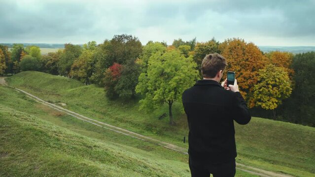 Blogger takes a picture of a beautiful autumn nature from a hill with his phone