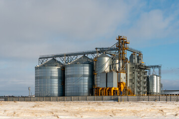Silver silos against the blue sky in winter. Grain storage in winter at low temperatures. Production for processing, drying, cleaning and storage of agricultural products, flour, cereals and grain