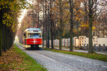 Obraz na płótnie Canvas Old vintage tourist tram comes through the alley of a Prague city in an autumn day. Electric transport connection. Prague tram network is third largest in a world. Retro historic electro transport