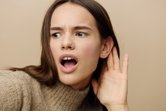 a funny, emotional, upset woman holds her hand near her ear, listening with her mouth wide open and looks with a puzzled expression on her face. Close horizontal, studio photography