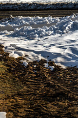 ripples in the snow next to muddy tire tracks
