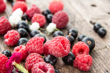 Ripe, juicy red raspberries and black currants are beautifully scattered on wooden boards.
