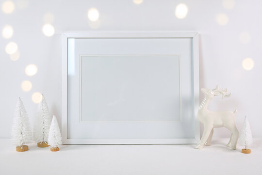 Christmas artwork print poster art picture frame mockup, styled with white reindeer and mini trees, bokeh party fairy lights on a minimalist white background.