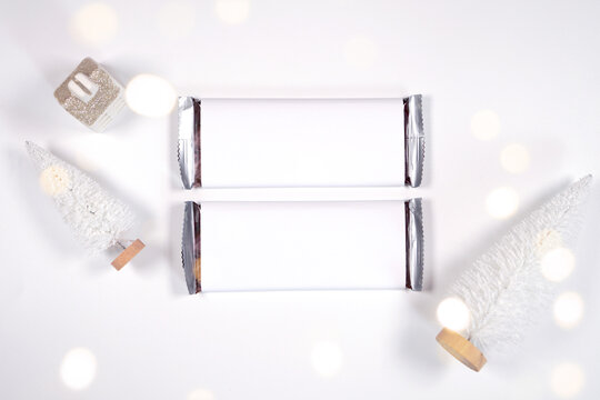 Christmas chocolate bar wrapper mockup, styled with white reindeer and mini trees, bokeh party fairy lights on a minimalist white background.