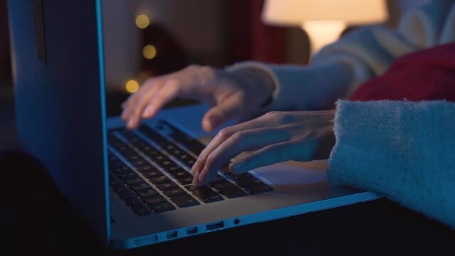Hands of young woman working with her laptop in the bed in the middle of the night. 4K slow motion.