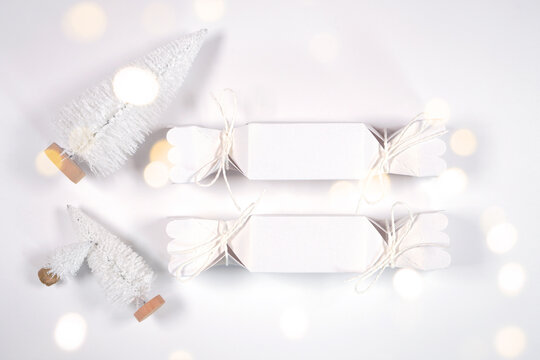 Christmas party treats favor boxes, Christmas Crackers mockup, styled with white reindeer and mini trees, bokeh party fairy lights on a minimalist white background.