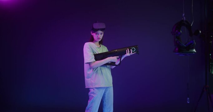 Woman in a virtual reality headset with a game gun in her hands in a VR studio