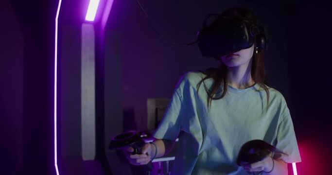 Woman in virtual reality headset playing video game with joystick controllers