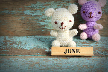 June text on wood block and couple of teddy bear crochet knitting on light blue painted old planks background. Hello June concept. Empty space for text