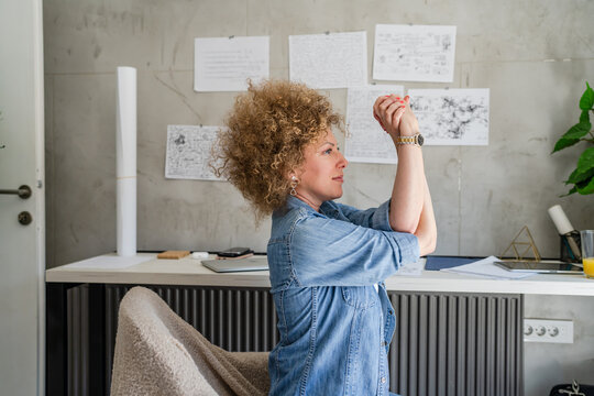 One woman adult mature caucasian female at her office desk sitting at work stretching arms Relaxation exercise Resting while taking a brake Workplace Concept copy space real people side view