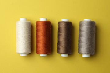 Different colorful sewing threads on yellow background, flat lay