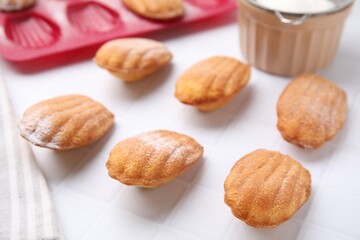 Delicious madeleine cookies and baking mold on white tiled table, closeup