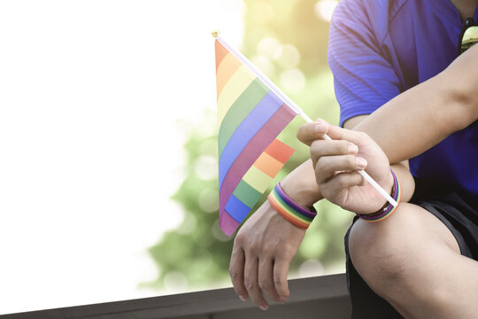 Rainbow Flag Holing In Hand Of Asian Gay Which Wears Rainbow Wristband To Call Out And Shows LGBT Gender Diversity And Respecting Gender Alternative Around The World.