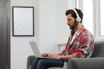 Handsome bearded man with headphones using laptop indoors