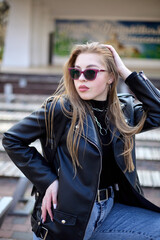 Outdoor portrait of a beautifull young woman in a black jacket and pink sunglasses