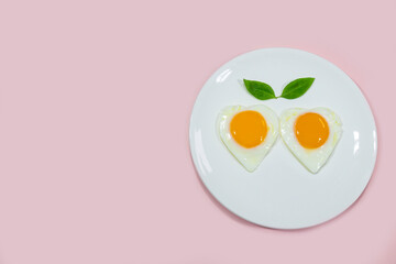 Fried eggs with heart-shaped leaves in white plate on a bright pink background message writing concept about love valentines day