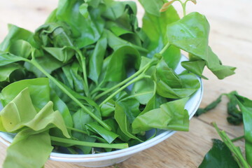 Gnetum gnemon leaves in a white bowl on a wooden table