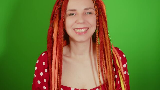 Young woman with dreadlocks looking at camera, smiling on green background. Portrait of female with bright hairstyle expressing positive emotion.