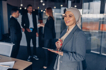 Smiling muslim businesswoman in hijab working on digital tablet while standing in modern office