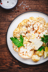 Baked cauliflower steak on plate, rustic wooden table background, top view