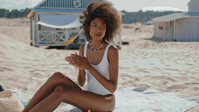 Beautiful girl applying suntan lotion on beach. Stylish woman sunbathing alone