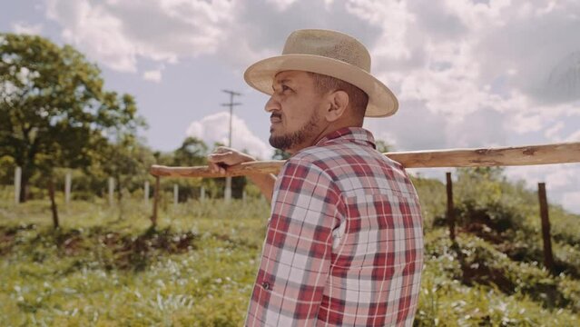 Portrait of young man in the casual shirt holding his hoe in the farm. Farm tool. Latin man. Premium Cinematic 4K