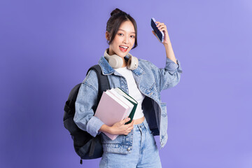 Portrait of a beautiful Asian schoolgirl wearing a backpack on a purple background