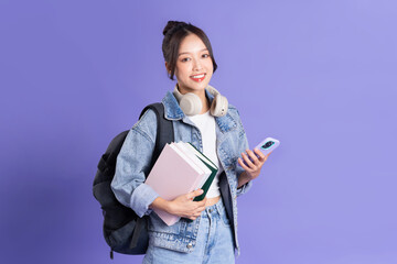 Portrait of a beautiful Asian schoolgirl wearing a backpack on a purple background