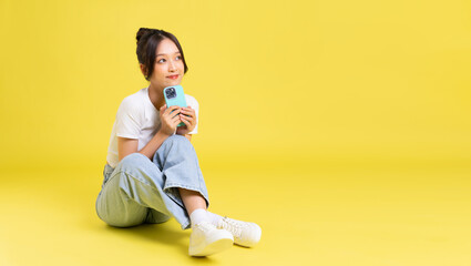 portrait of a beautiful young asian girl sitting on a yellow background - obrazy, fototapety, plakaty