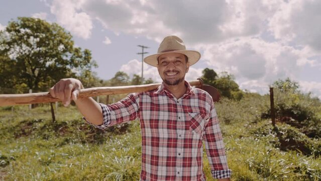 Portrait of young man in the casual shirt holding his hoe in the farm. Farm tool. Latin man. Premium Cinematic 4K