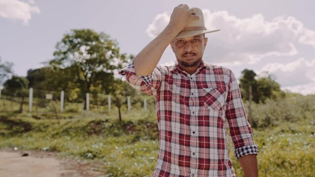 Portrait of young man in the casual shirt taking off hat in the farm on the colorful sky background. Premium Cinematic 4K