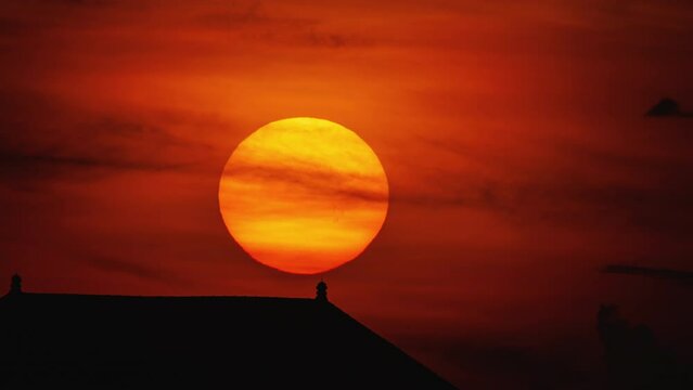 big sun timelapse and cloudless sky sunset over the rooftops of typical Balinese city houses, location Bali Indonesia
