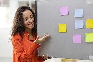 Smart and active latin woman showing and holding different colored sheets of note papers, ready for message on refrigerator in kitchen. Anywhere can work, lifestyle with technology concept