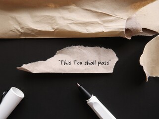 Torn office envelope with handwritten text THIS TOO SHALL PASS, self reminder mantra that nothing,...