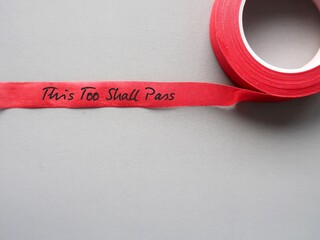 Red tape on gray copy space background with handwritten text THIS TOO SHALL PASS, to remind...