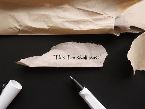 Torn office envelope with handwritten text THIS TOO SHALL PASS, self reminder mantra that nothing, good or bad, lasts forever; all circumstances are temporary