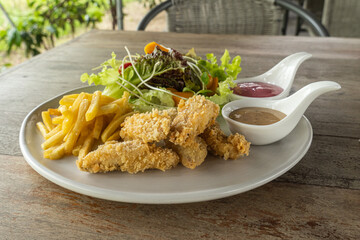 Battered fish steak on a white plate was salad and salad dressing on the side of the dish. on the wooden table.