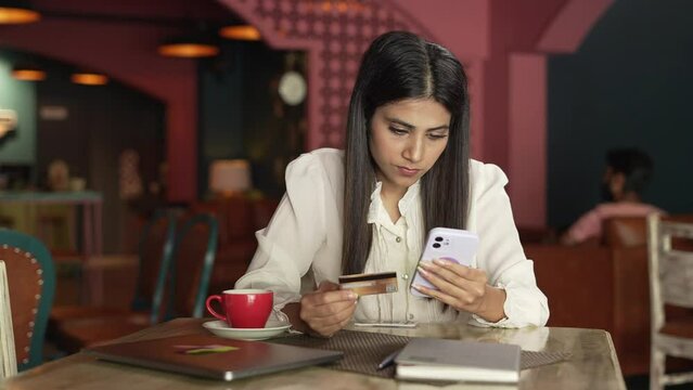A Indian lady doing online payment using her bank ATM card - an online transaction, banking, and finance. Asian pretty girl doing online shopping using her debit credit card using on the smartphone.