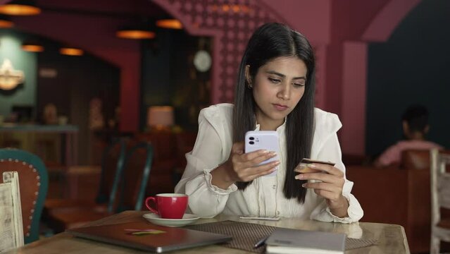 A Indian woman is entering debit credit card details - online shopping, e-commerce website, discounts. young Asian lady is making online payment - using on the smartphone and drinking coffee.