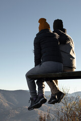 Young couple from behind is sitting above mountains view and looking away
