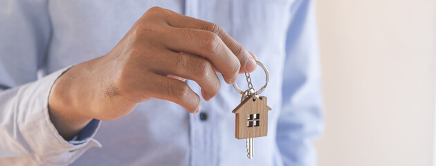 Home agent, broker man in suit standing, realtor holding the house key to hand over to new...