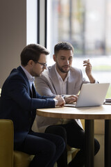 Two young 35s office colleagues review collaborative task, discuss on-line business common project...