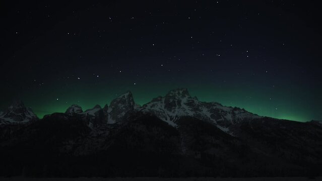 Northern Lights (Aurora Borealis) are dancing on the night sky above the snowy mountain peaks. Time Lapse. 