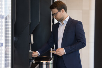 Young businessman in suit pours favourite beverage, uses vending machine in office cafeteria or self-service automated retail place for comfort and busy life, start working day with cup of hot coffee - obrazy, fototapety, plakaty