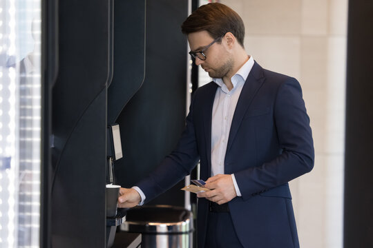 Young businessman in suit pours favourite beverage, uses vending machine in office cafeteria or self-service automated retail place for comfort and busy life, start working day with cup of hot coffee